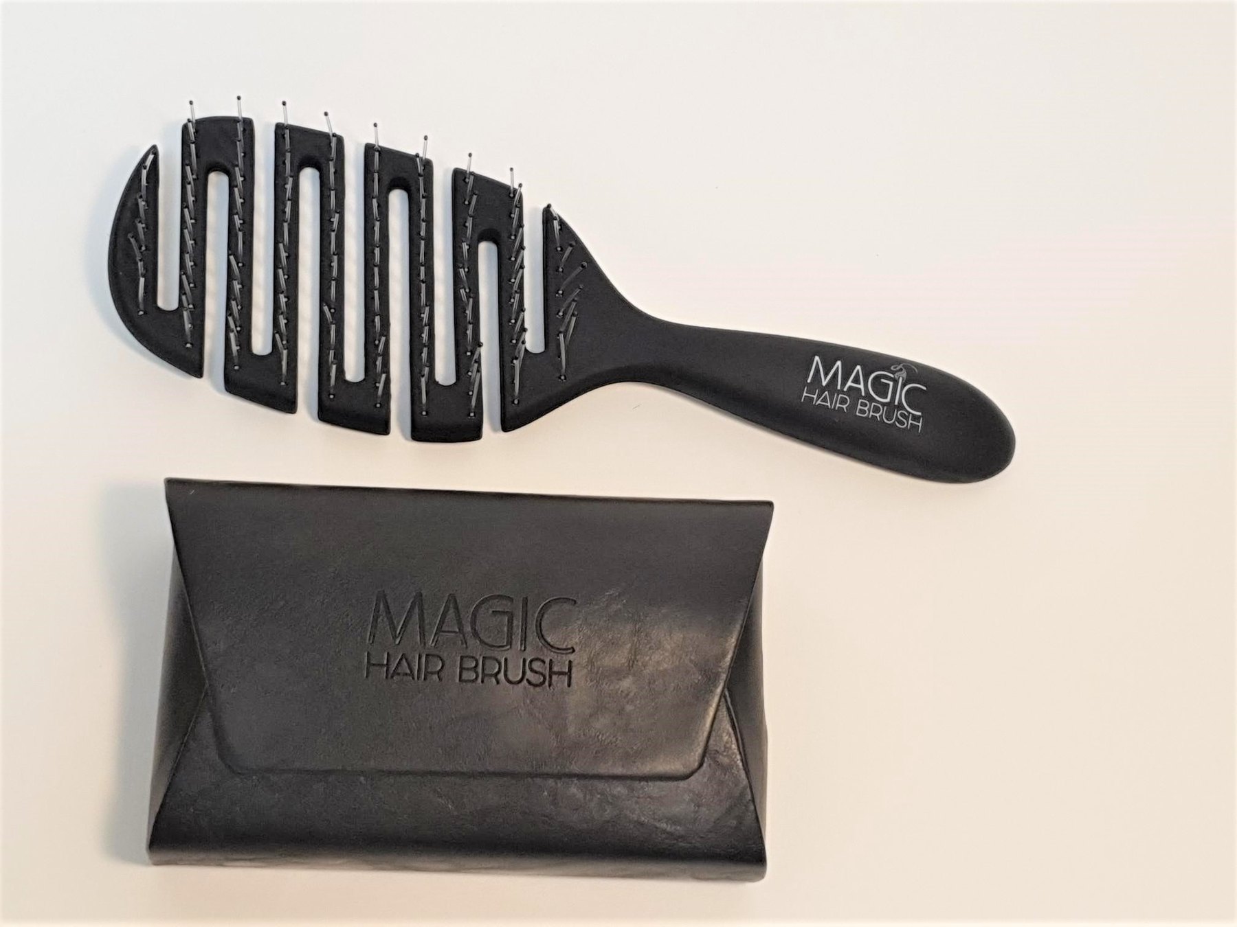 The black Magic Hair Brush photographed from above beside its embossed black wallet, showing the six flexible fingers and the open slots between them.